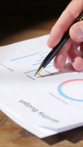 Person tracking budget with pen and paper.